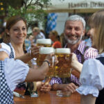 Der Zeughaus Biergarten in Augsburg - Drei Frauen und ein Mann in Tracht trinken Bier aus Maßkrügen
